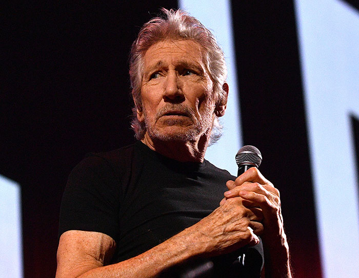 Roger Waters holding a microphone on stage, delivering a passionate speech during a live performance. Roger Waters holding a microphone on stage, delivering a passionate speech during a live performance.