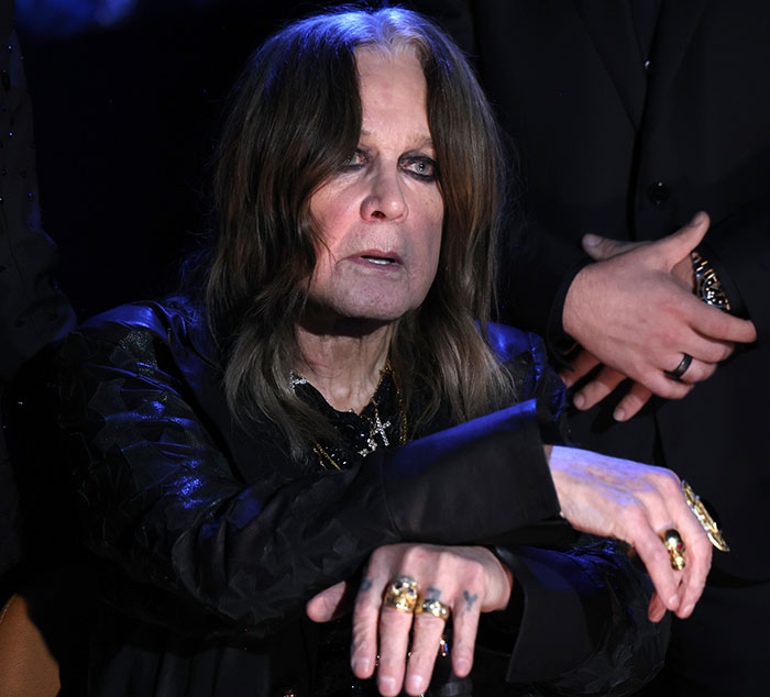 Ozzy Osbourne wearing rings and dark clothing with a serious expression amid a dramatic low-light setting. Ozzy Osbourne wearing rings and dark clothing with a serious expression amid a dramatic low-light setting.