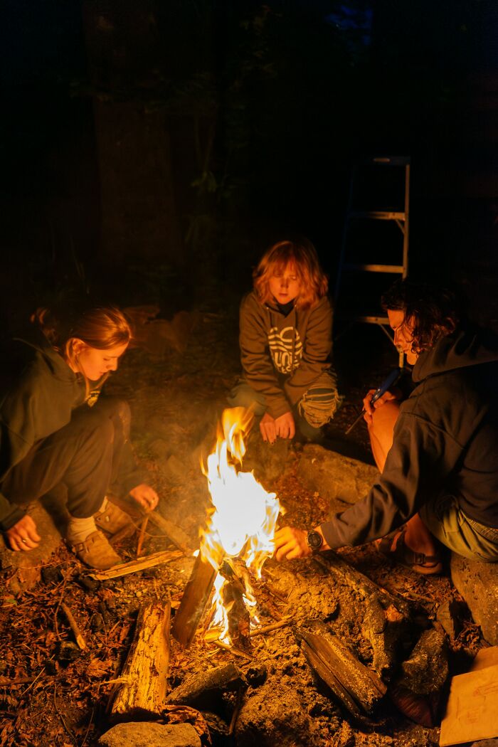 Three people sitting around a campfire in the dark woods, perfect setting for creepy stories at night.