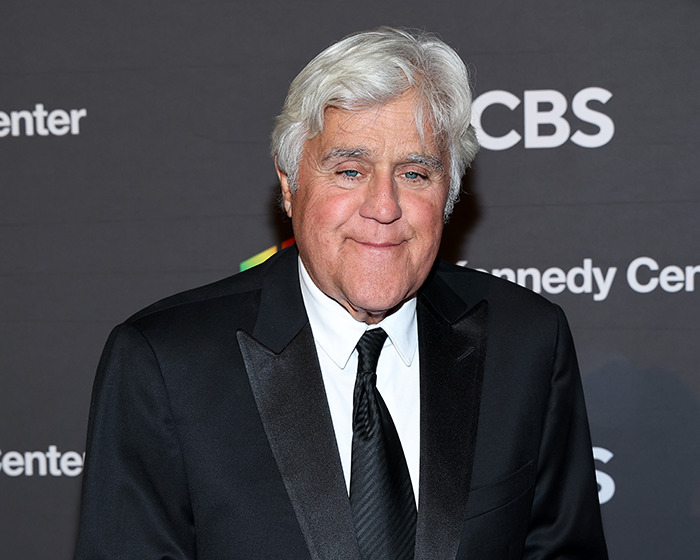 Jay Leno wearing a black suit and tie, posing at a media event, reacting to Jimmy Kimmel suspension comments.