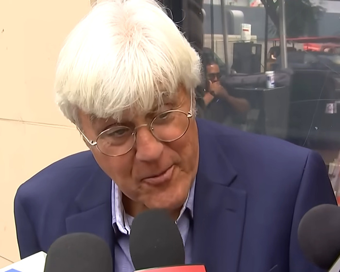 Jay Leno speaking to reporters wearing glasses and a blue suit jacket reacting to Jimmy Kimmel's suspension comments.
