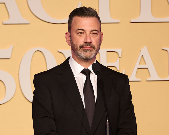 Jimmy Kimmel in a black suit and tie speaking at a podium, related to suspension after offensive Charlie Kirk comments.