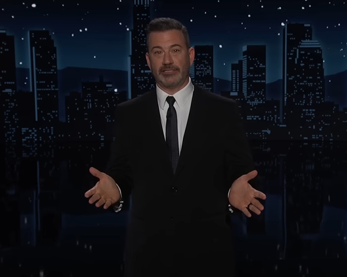 Jimmy Kimmel in a dark suit on a nighttime cityscape set, addressing the audience about suspension and controversy.
