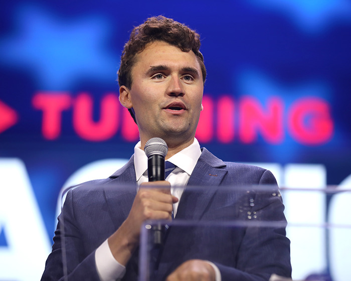 Man in a suit speaking into a microphone at a podium, related to Jimmy Kimmel suspension and Charlie Kirk comments.