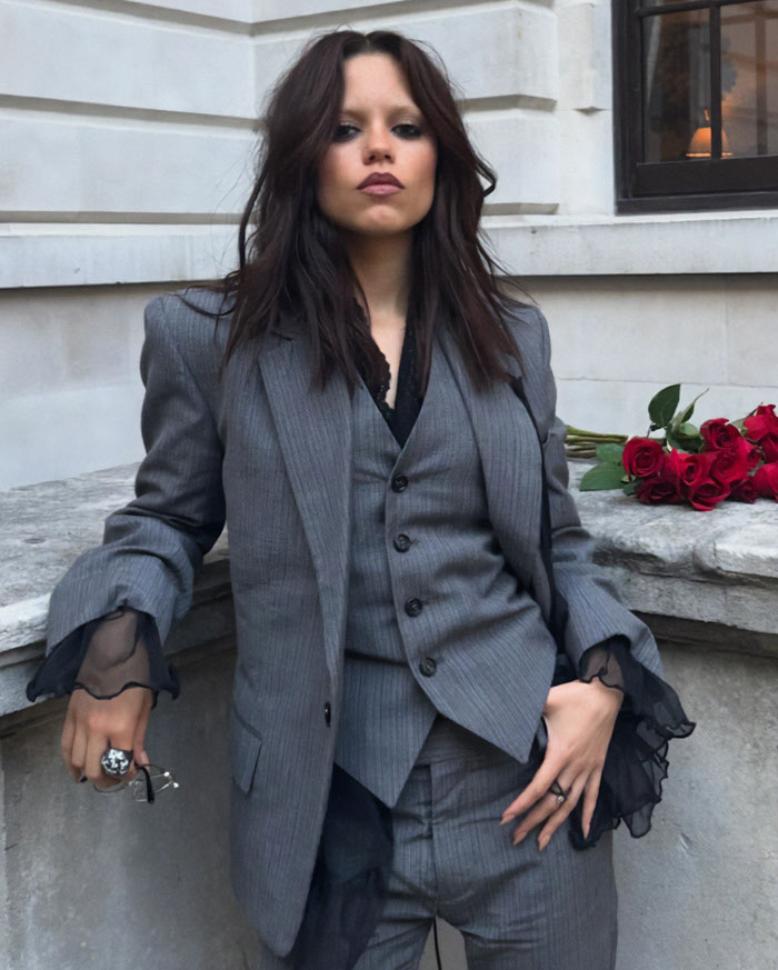 Jenna Ortega in a tailored gray suit with sheer sleeves, showcasing a risky diamond-encrusted look at a stylish event. Jenna Ortega in a tailored gray suit with sheer sleeves, showcasing a risky diamond-encrusted look at a stylish event.