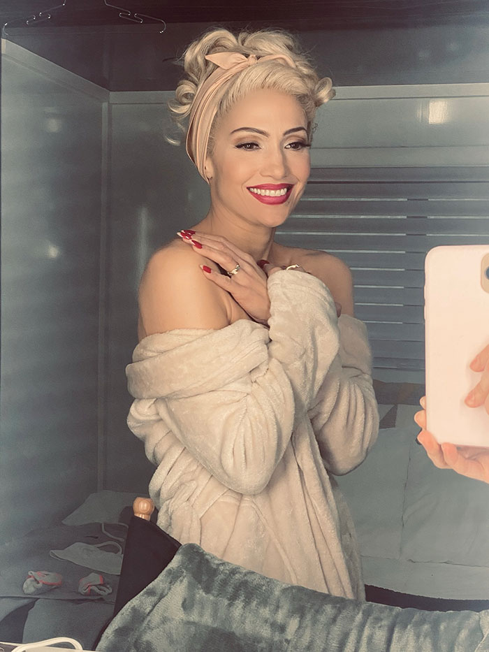 Blonde woman with vintage curls and red lipstick smiling in a mirror selfie, fans mistaking Jennifer Lopez for Gwen Stefani.