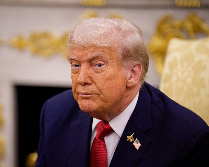 Donald Trump in a suit and red tie sitting in an official room with gold decor, related to ABC lawsuit and Jimmy Kimmel.