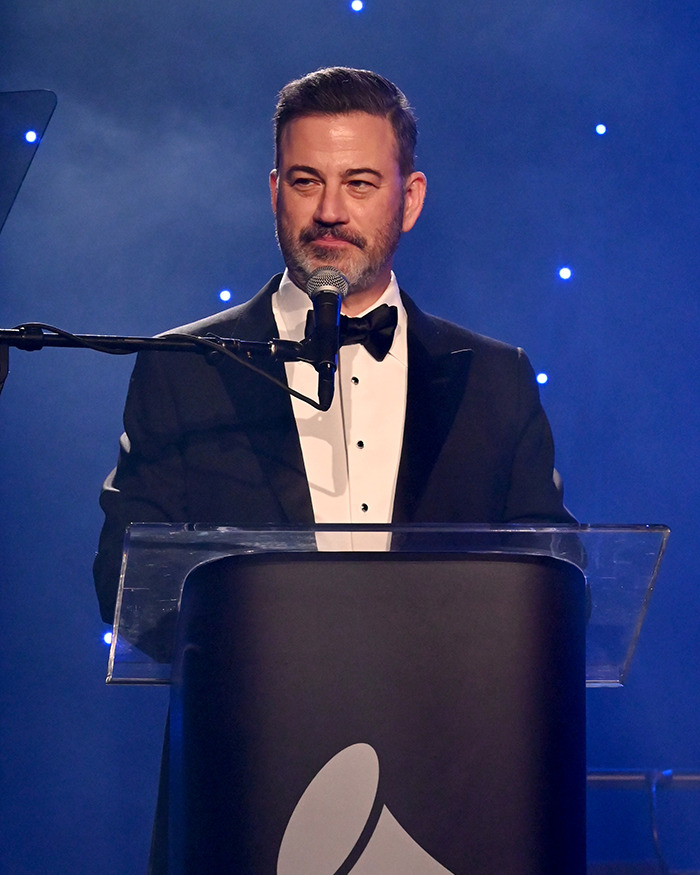 Jimmy Kimmel speaking at a podium in a tuxedo, firing back at Trump over ABC lawsuit threat during comeback event.