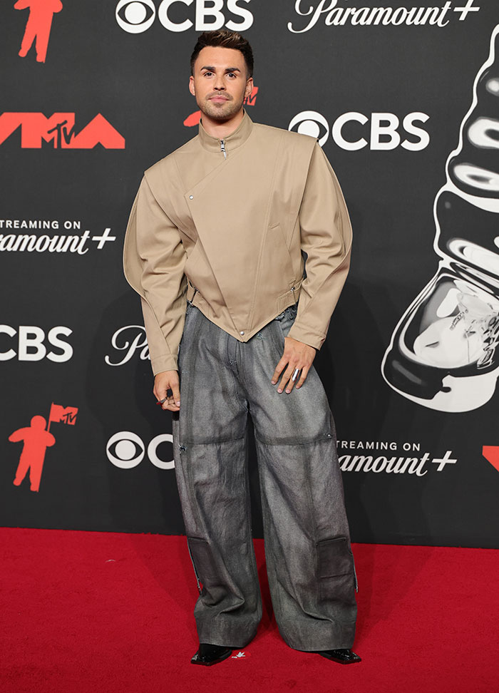 Man wearing oversized beige jacket and wide gray pants posing on the red carpet at the 2025 Video Music Awards worst dressed stars.
