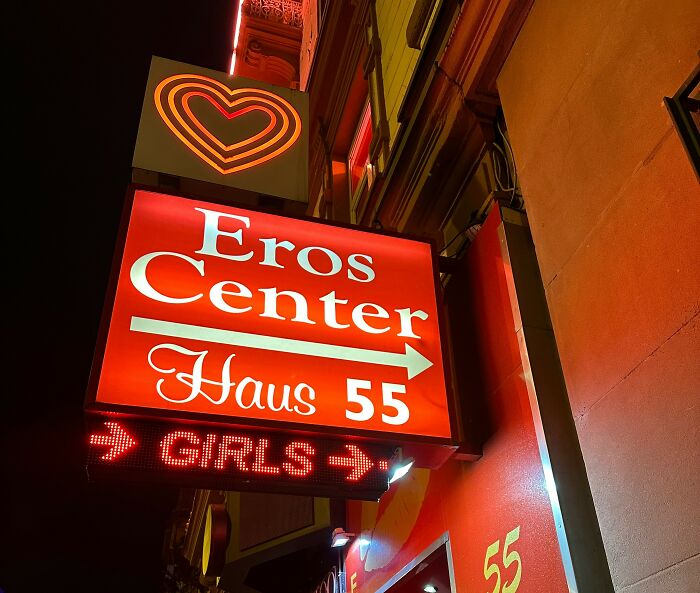Neon sign at night reading Eros Center Haus 55 with arrows and glowing heart, symbolizing shocking family secrets revealed.