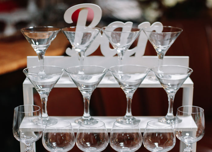 Clear wine and martini glasses arranged on a bar stand, symbolizing celebrations at a white wedding dress event.