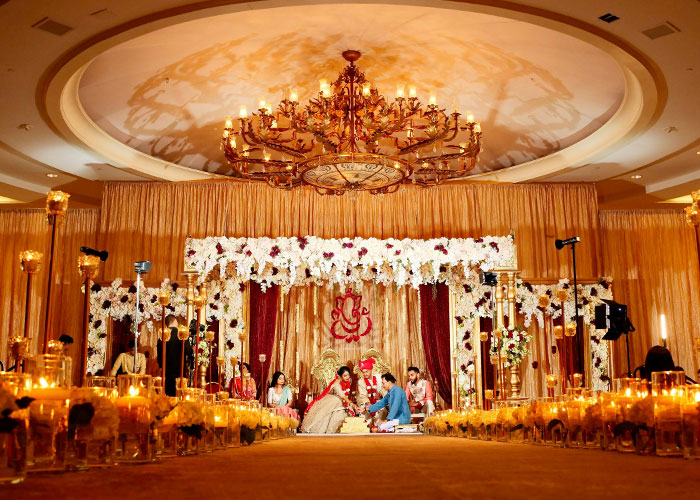 Elegant wedding ceremony setup with floral decorations and a bride in a white wedding dress under a grand chandelier.