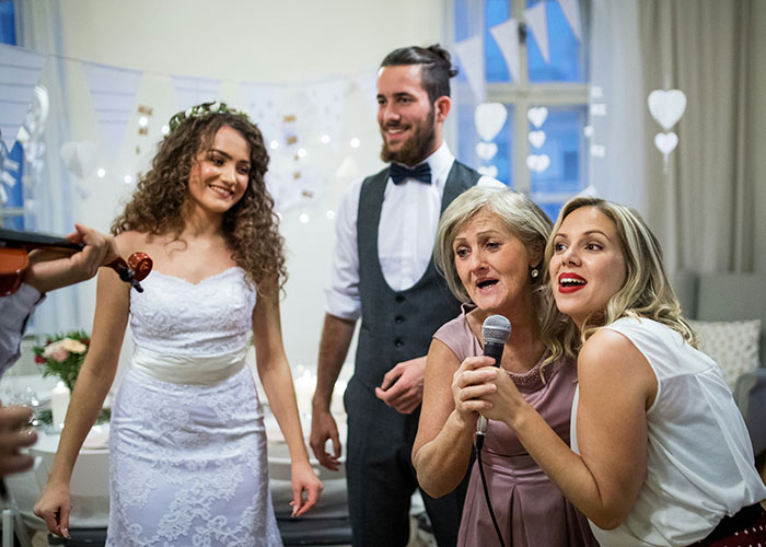 Bride in a white wedding dress smiling while guests enjoy music and karaoke at a lively wedding celebration.