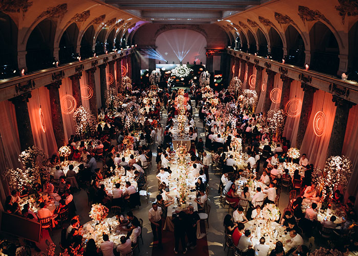 Large wedding reception with guests seated at decorated tables under warm lighting, showcasing an elegant white wedding dress event.