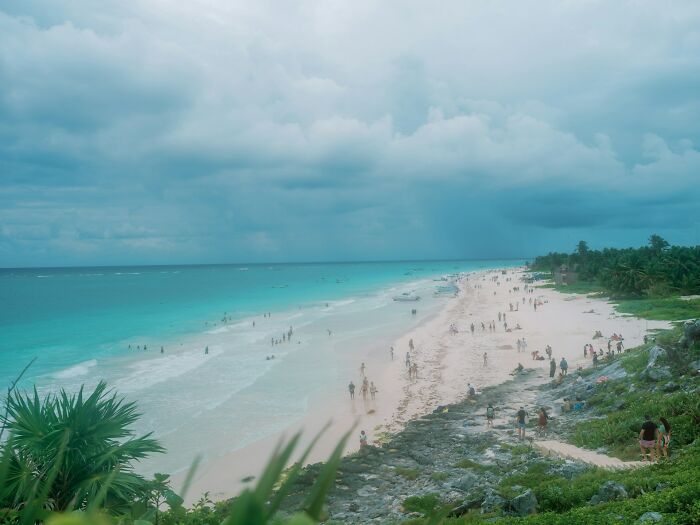 Crowded tropical beach with turquoise water and cloudy sky showing travel destinations not as pictured in photos.