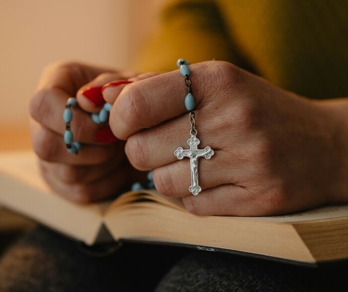 Hands holding a rosary over an open book, illustrating real-life stories of people transforming into what they once hated.
