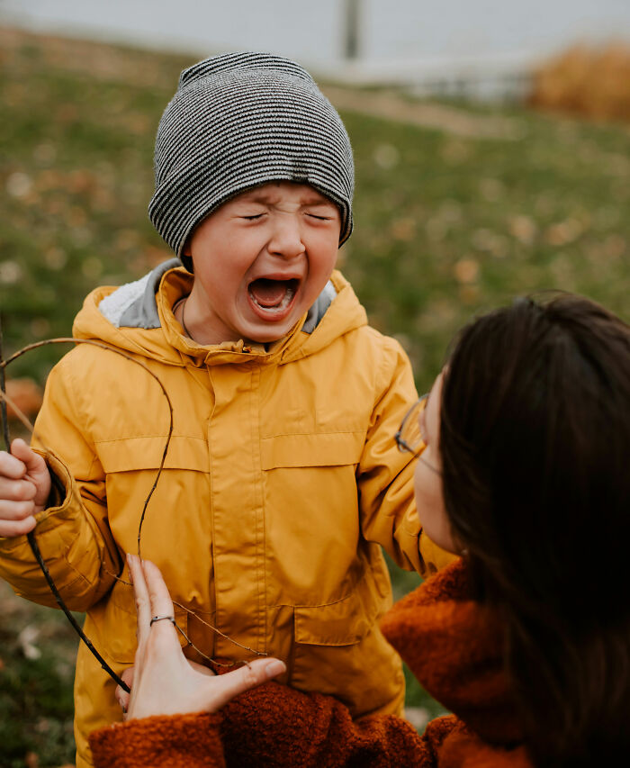 Child in yellow jacket crying outdoors while adult comforts them, illustrating parenting hacks to save sanity.
