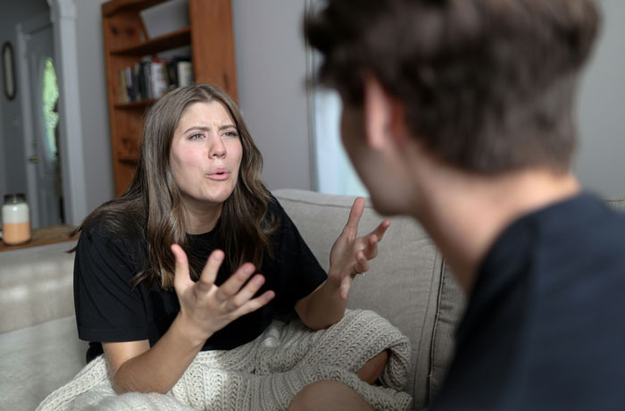 Couple arguing on couch about roommate conflict after kid was allowed to sleep in roommate&rsquo;s bed.