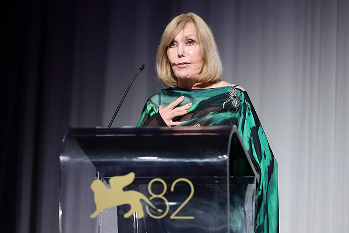 Kim Novak in a green dress speaking at a podium during a lifetime achievement award ceremony at Venice Film Festival.