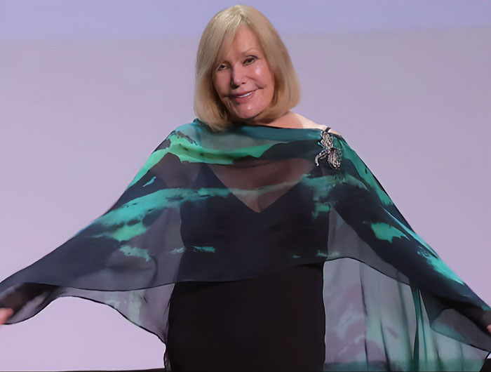 Kim Novak on stage wearing a flowing green and black shawl, receiving a lifetime achievement award at a film festival.