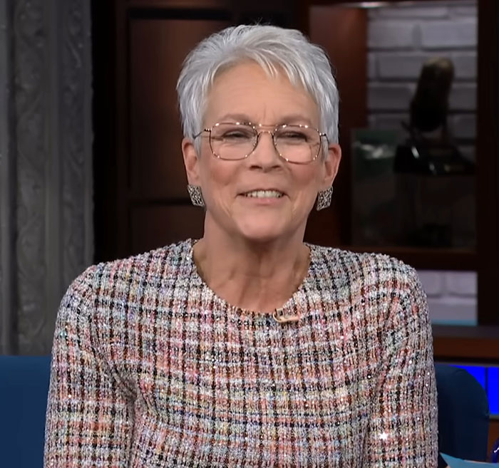 Smiling woman with short white hair and glasses wearing a patterned top in an indoor interview setting about celebrities before fame.
