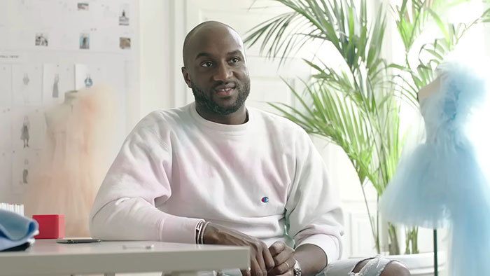 Man in a casual white sweatshirt sharing stories about celebrities before fame in a bright, plant-filled room.