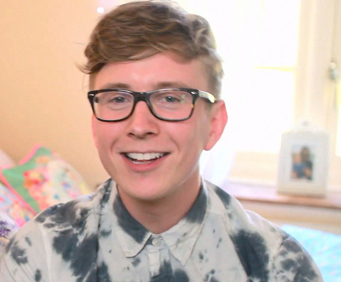 Young man with glasses smiling indoors, representing people who knew celebrities before fame sharing stories.