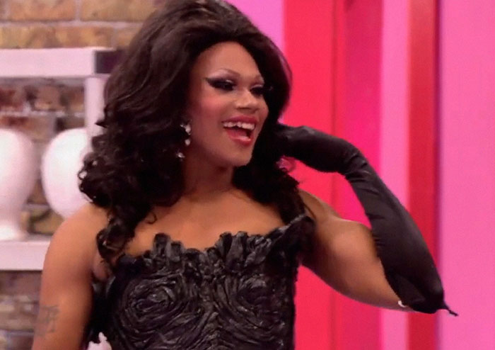 Drag queen in black dress and gloves smiling confidently, featured in stories about people who knew celebrities before fame.
