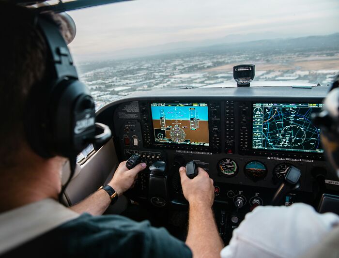 Pilot controlling an aircraft cockpit with navigation screens visible, unrelated to butcher and gravedigger professions.