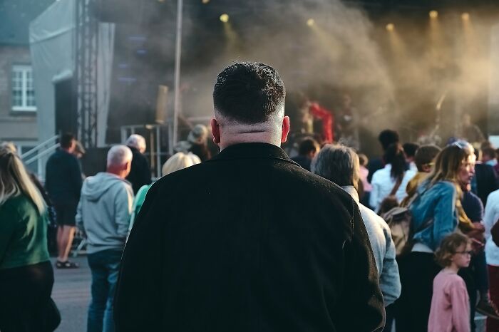 Man with short hair and black jacket standing in a crowded outdoor event, reflecting on traveling to the Bahamas complaints.