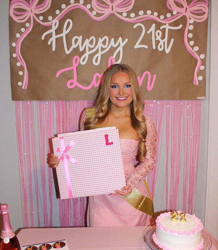 Young woman in a pink dress celebrating a birthday, holding a gift box with pink ribbons and decorations.