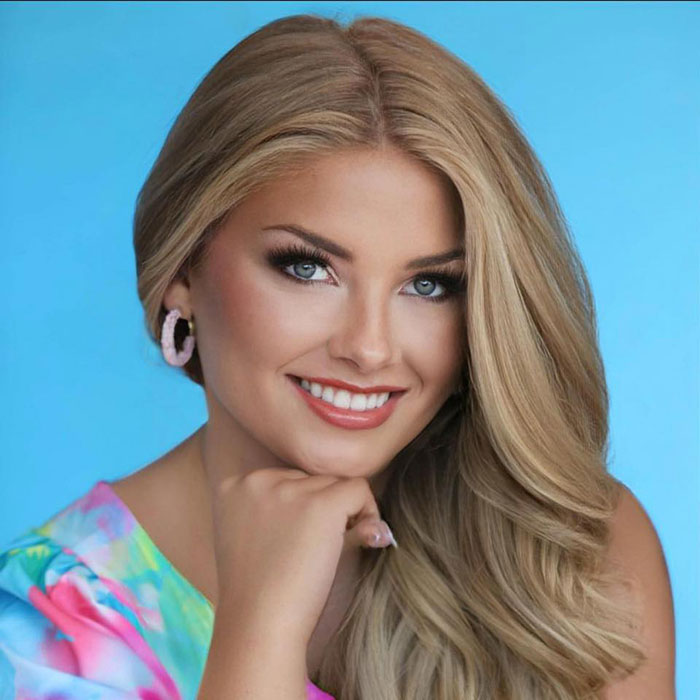 Young woman smiling with long blonde hair against blue background, related to social media posts about motherhood and hidden baby body.