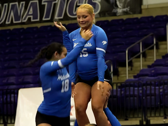 Cheerleader with visible baby belly performing during a routine in volleyball arena wearing blue uniform. Cheerleader with visible baby belly performing during a routine in volleyball arena wearing blue uniform.