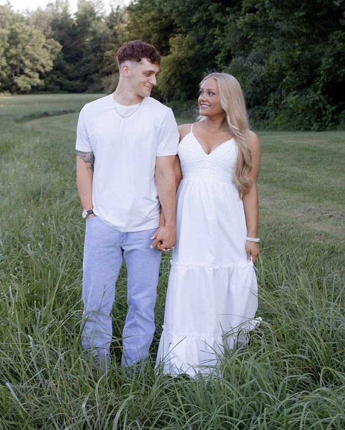 Young couple holding hands outdoors in a grassy field with trees in the background on a sunny day
