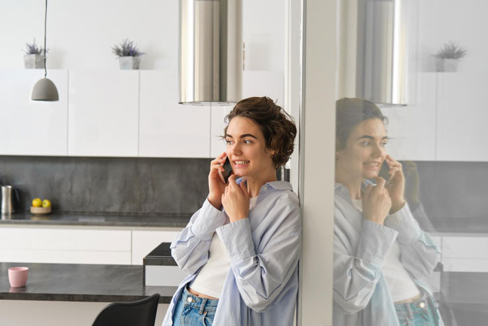Young woman smiling and talking on phone in modern kitchen, reflecting landlord malicious compliance drama concept.