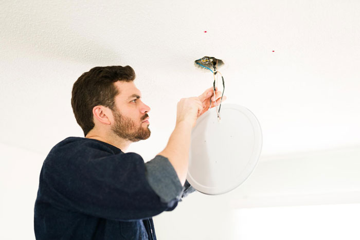 Man repairing ceiling light fixture, demonstrating landlord malicious compliance during home maintenance situation.