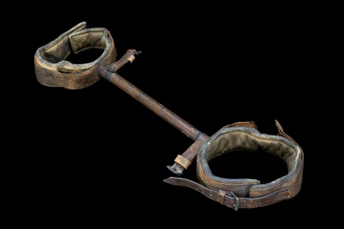 Vintage medical restraint device with padded leather cuffs connected by a metal rod, showcasing old-school medical equipment.