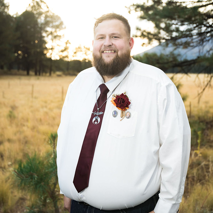 Man with beard outdoors wearing white shirt and burgundy tie, symbolizing man declared legal father of his brother.