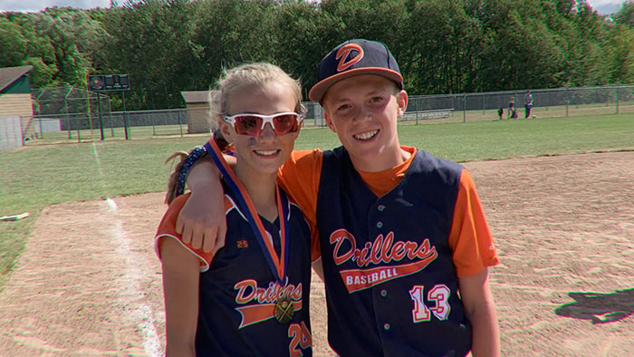 Two young baseball players in Drillers uniforms smiling on the field, illustrating a broken person family story.