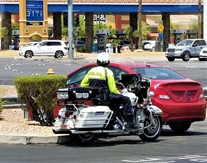 Police officer on motorcycle pulls over a red car at a gas station, highlighting cases of innocent people blamed by police.