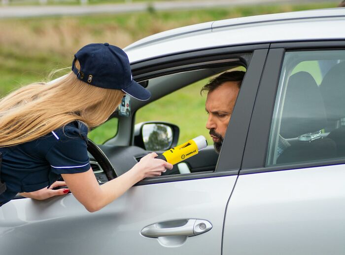 Police officer administering breathalyzer test to driver in a car, illustrating lawyers and cops revealing incriminating mistakes.