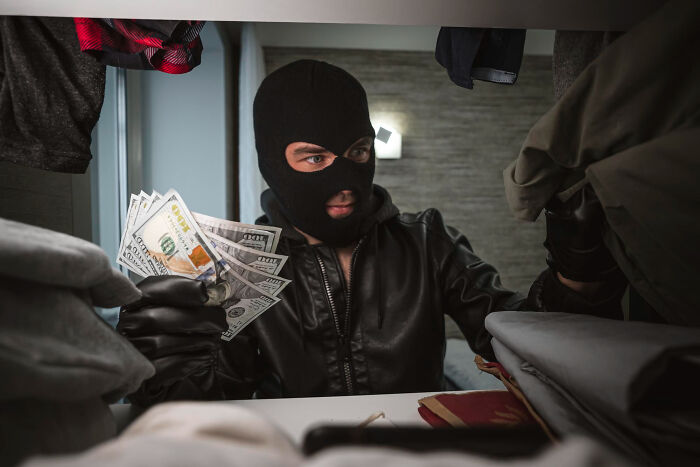 A masked man in black leather jacket holding cash inside a closet, illustrating how people incriminate themselves.