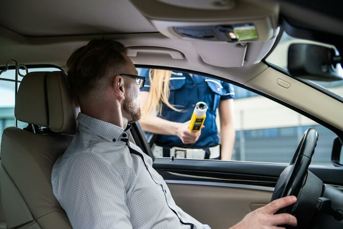Man sitting in car being tested by police officer with breathalyzer, illustrating lawyers and cops on incriminating actions.