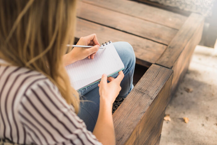 Person sitting on a wooden bench, writing notes in a notebook, depicting lawyers and cops discussing incriminating cases.