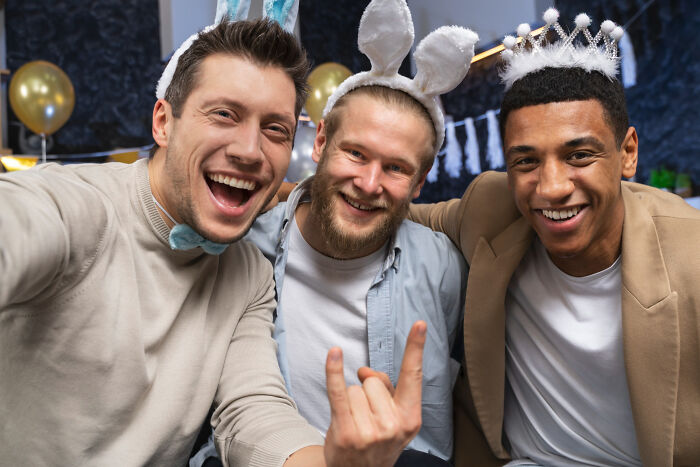 Three friends wearing bunny ears and crowns, having fun and laughing at a casual party setting.