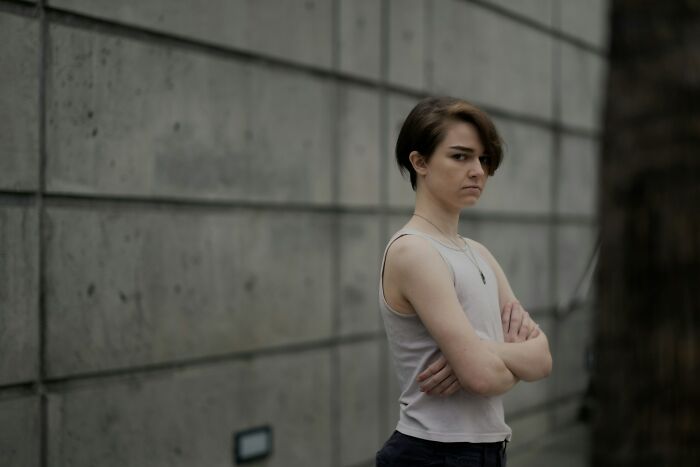 Young adult with crossed arms and serious expression standing against a concrete wall, illustrating adults who struggle with growing up.