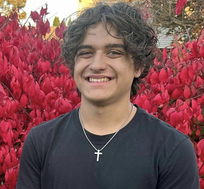 Teenage boy smiling outdoors in front of autumn red leaves, related to viral TikTok trend injuries and incidents.