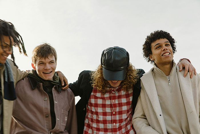Group of young men standing close together outdoors, smiling and enjoying time despite awkward boxer-related moment.