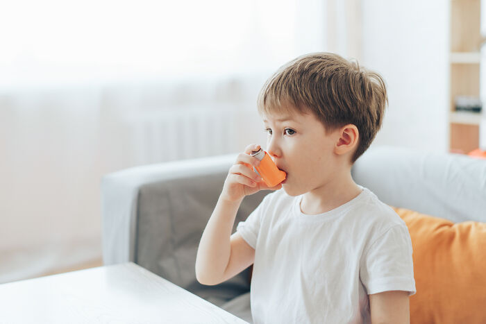 Young boy using an orange inhaler while sitting indoors, illustrating common reactions to advanced stupid out-of-touch moments.