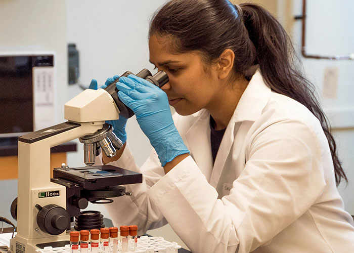Female scientist in a lab coat using a microscope, surrounded by test tubes, exploring interesting scientific facts.